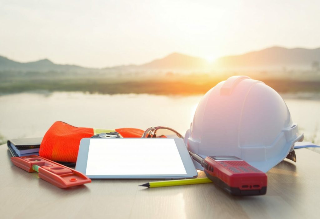 A hard hat, level, tablet and other tools sit on the ground, basked in the light of a sunset, indicating that every industry can benefit from changing with the times.