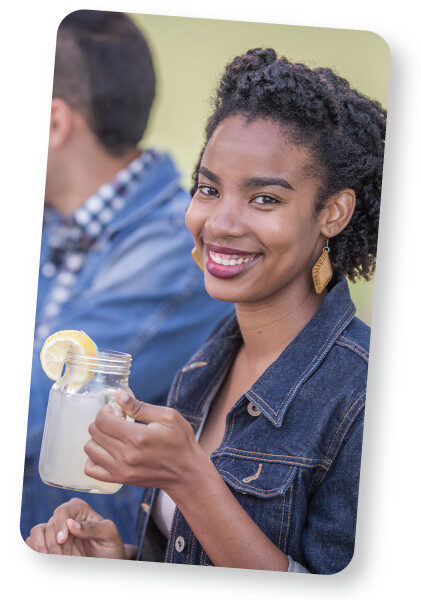 Image of woman smiling with a mug of ice cold lemonade in her hand.