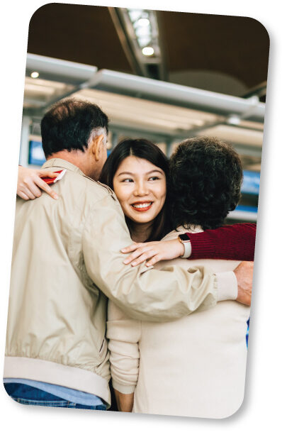 Photo of adult child and parents hugging in an airport.