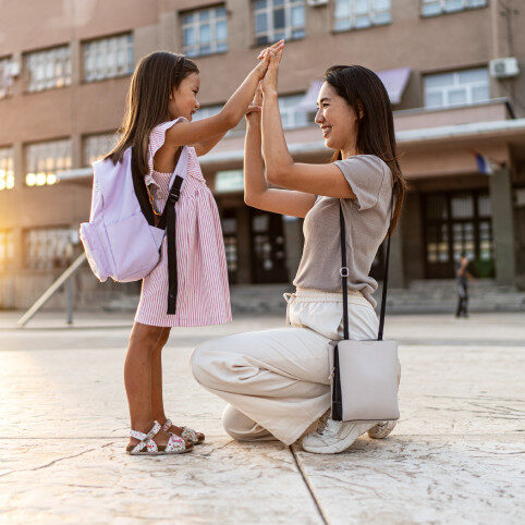 Mother with daughter wearing a backpack outside of school building.
