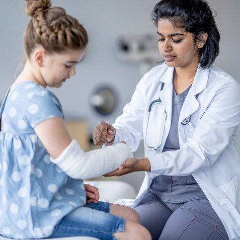 Little girl sitting while a doctor adjusts her cast.