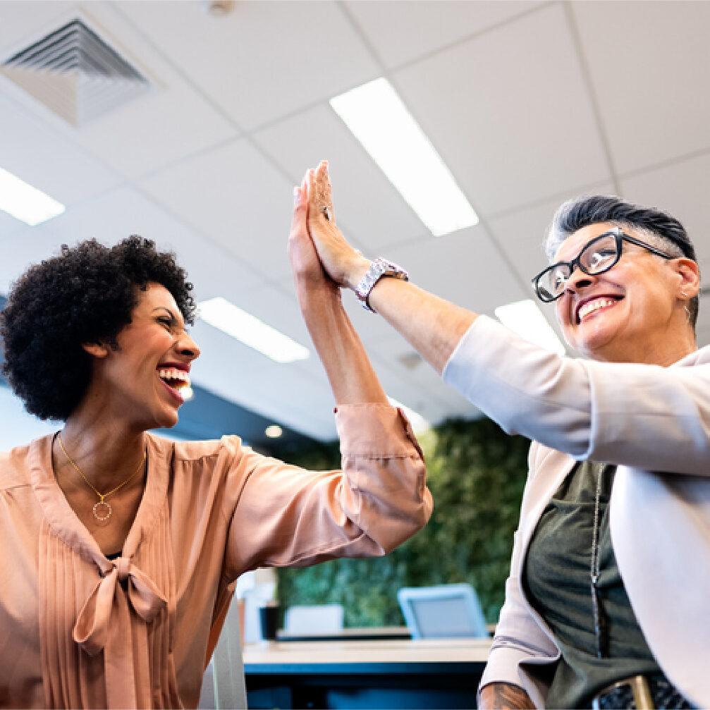 Two professionals smiling and high-fiving in an office.