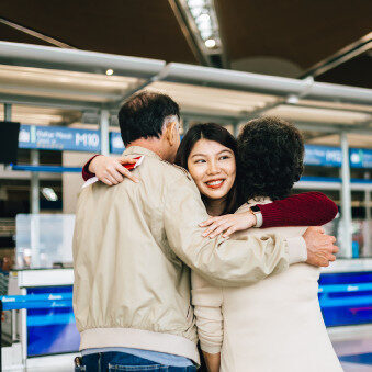 Parents and their smiling daughter hugging at the airport.